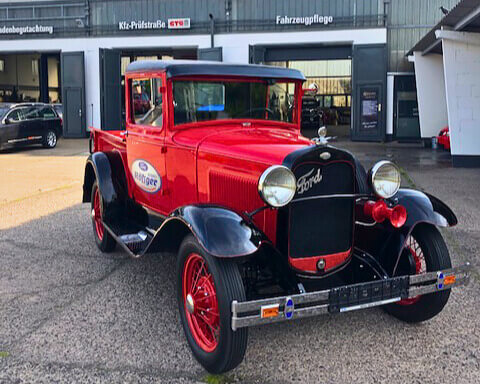Dresden-Gutschein-Distrex-05 Ein restaurierter, leuchtend roter Ford-Oldtimer mit schwarzen Kotflügeln steht auf dem Außengelände vor den Werkstatthallen.