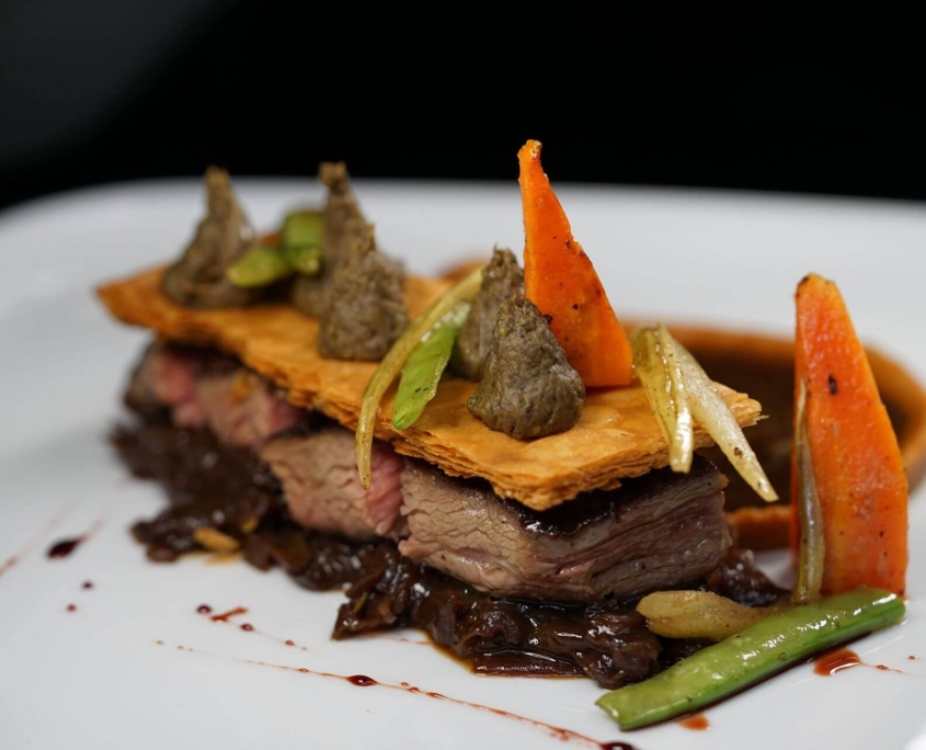 Rindfleisch mit Kruste, Karotten und Sauce auf weißem Teller im Restaurant Petit Frank Dresden.