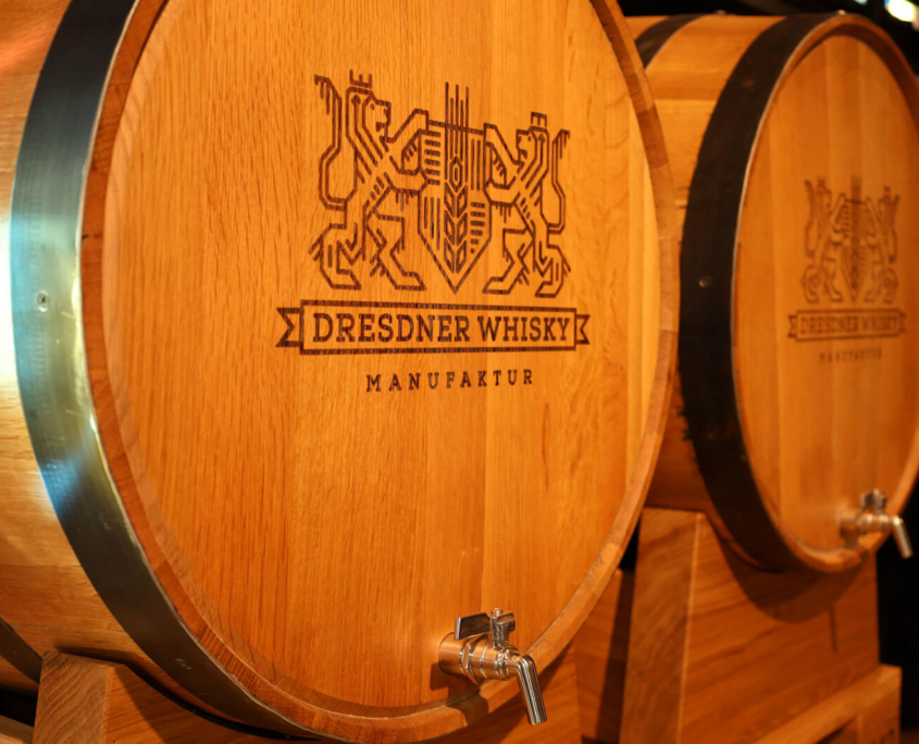 Dresdner Whisky Manufaktur 02 Detailaufnahme von zwei hölzernen Eichenfässern mit dem eingebrannten Logo der Dresdner Whisky Manufaktur und silbernen Zapfhähnen zur Fassabfüllung.