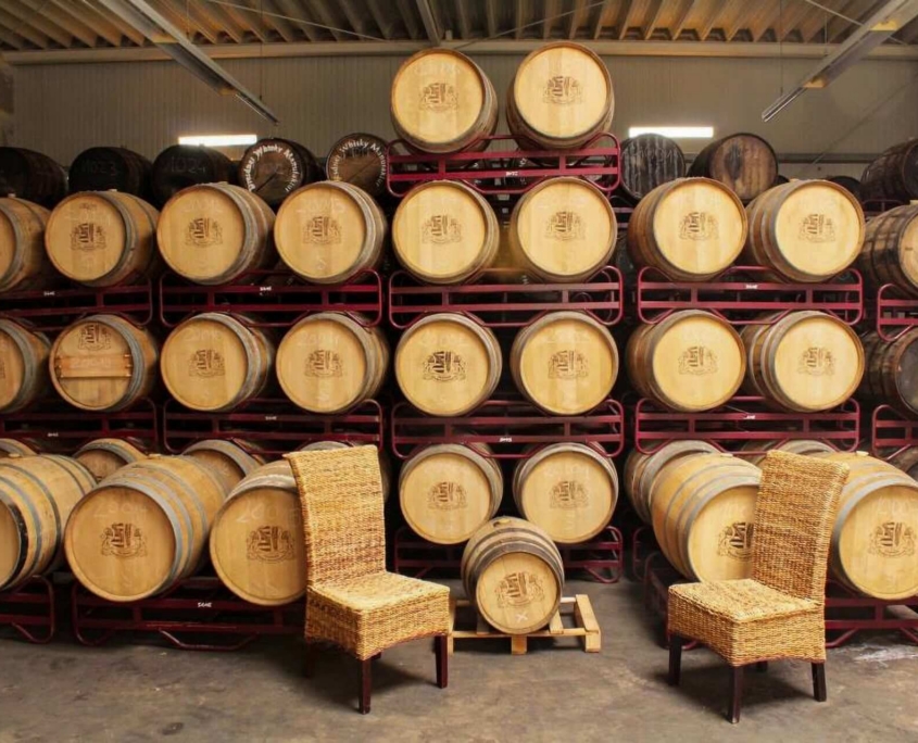 Dresdner Whisky Manufaktur 06 Holzfässer mit Whisky in einem Fasslager der Dresdner Whisky Manufaktur, zwei Stühle für Tastings im traditionellen Lagerhaus.